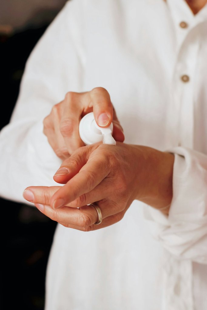 Hands applying lotion from a white pump to soothe dry hands