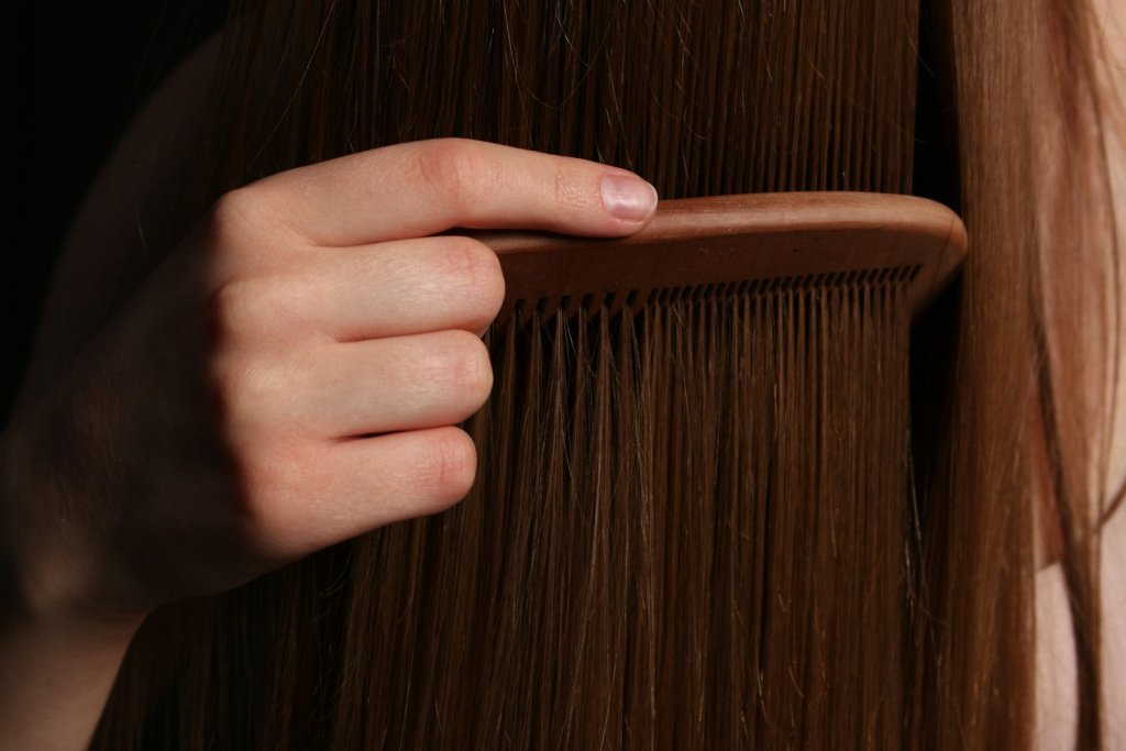 A hand gently combing long brown hair as part of a healthy scalp care routine