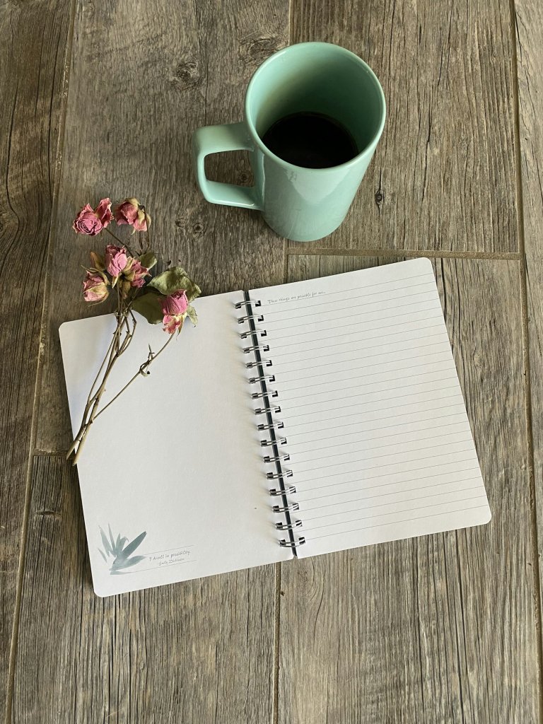 Notebook beside a ceramic mug on a wooden table, a quiet moment for self-compassion practice